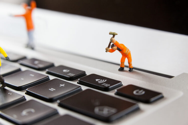 Conceptual image of miniature workmen repairing a laptop keyboard